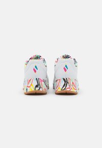 Das Schuhwerk hat ein weißes Obermaterial, bunte abstrakte Muster auf der Sohle und einen strukturierten Kragen mit mehrfarbigen Akzenten.