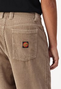 Kamisole byxor i ljusbrun med ribbad textur, med en bakficka prydd med en svart och röd "Santa Cruz" logotyp patch.