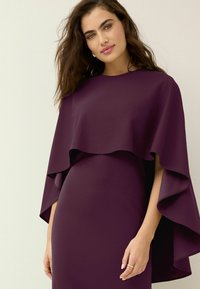 Paarse jurk met een vloeiende, gelaagde cape-ontwerp. De gladde textuur en de getailleerde silhoutte benadrukken de elegante vorm en kleur.
