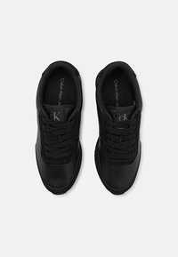 Baskets noires Calvin Klein avec lacets, dessus en cuir texturé et semelles intérieures marquées, vues de dessus sur un fond uni.