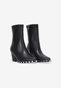 Botines de cuero negro hasta el tobillo con puntera cuadrada, tacón de altura media, cremallera lateral y tachuelas decorativas plateadas a lo largo de la suela.