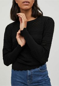 Zwart gebreid sweater met een textuurpatroon en gegolfde manchetten, gecombineerd met hoge blauwe denim jeans.