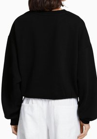 Sudadera negra recortada con cuello redondo, mangas oversized y una textura suave, combinada con pantalones blancos que cuentan con bolsillos traseros.
