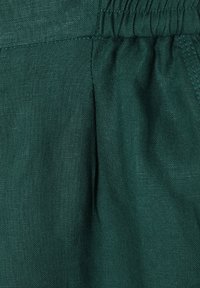 Tissu en lin vert foncé avec une surface texturée, présentant des plis et un élastique à la taille pour un ajustement décontracté et relaxé.