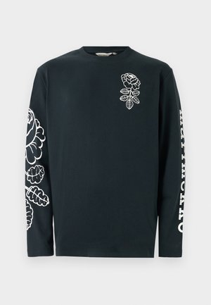 Camiseta negra de manga larga hecha de algodón, con diseños florales blancos en el pecho y en la manga izquierda, y texto a lo largo de la manga derecha.