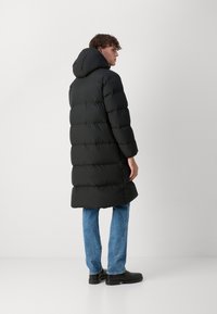Black puffy coat with a hood, featuring a quilted design and long sleeves, paired with blue jeans and black boots.