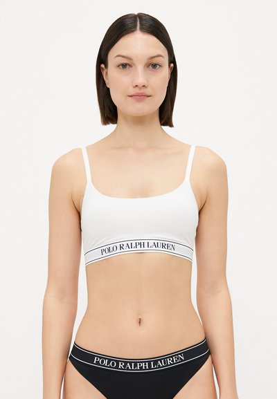 Fehér bralette vékony pántokkal és fekete derékpánttal, amelyen fehér betűkkel "POLO RALPH LAUREN" felirat található, sima textúrájú, egyszerű dizájnnal.