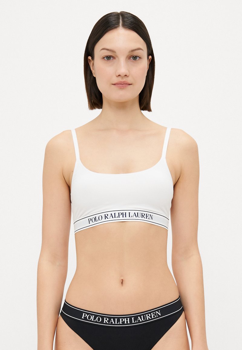 Hvit bralette med tynne stropper og en svart midjebånd med "POLO RALPH LAUREN" i hvit tekst, glatt tekstur, enkelt design.