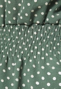 Tessuto verde con pois bianchi, con una superficie texture e una vita elastica arricciata. Design fluido.