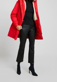 Rode gewatteerde jas met een fluffy binnenvoering, gecombineerd met zwarte strakke leren broek en donkerblauwe hoge enkellaarzen.