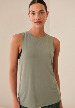 Top fără mâneci de culoare verde măsliniu, confecționat dintr-un material moale, având un guler rotund și o croială lejeră, purtat cu un sutien sport de culoare închisă dedesubt.