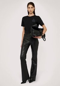 Czarny, dopasowany t-shirt z grafiką, zestawiony z czarnymi, skórzanymi, rozkloszowanymi spodniami z wysokim stanem. Modelka trzyma elegancką, czarną torebkę.