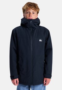 Schwarze wasserdichte Jacke mit Frontreißverschluss, verstellbarem Kapuze und einem Logo-Patch auf der linken Brust. Glatte Textur und lange Ärmel.