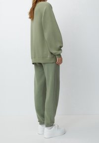 Olijfgroene sweatshirt en bijpassende trainingsbroek van zachte stof. De outfit heeft een ontspannen pasvorm, verlaagde schouders en ribgebreide manchetten.