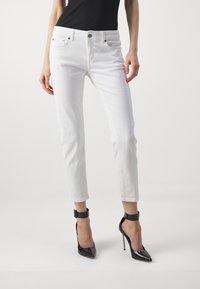 Valkoiset farkut, joissa on kapea malli, keski-korkea vyötärö, viisi taskua ja hentoa tikkausta, yhdistettynä mustiin korkokenkiin.