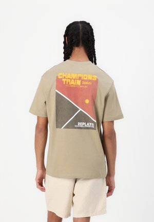 Light beige t-shirt with a graphic print on the back featuring red, yellow, and black geometric designs. Cotton fabric, short sleeves.