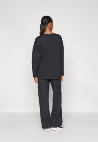 Zwarte oversized sweatshirt en cargobroek van zacht materiaal, met zijzakken en een ontspannen pasvorm. Mix van casual elementen en comfort.