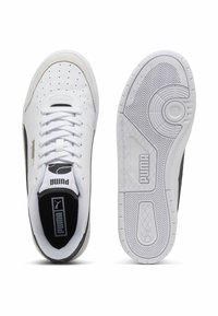 White leather sneakers with perforated toe, black accents, and a textured rubber sole. Features lace closure and logo detailing on tongue.