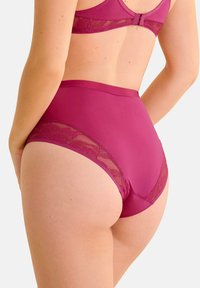 Culottes fuchsia taille haute avec des accents en dentelle florale sur les côtés. Texture lisse avec un léger éclat. Conçus pour le confort et une couverture complète.