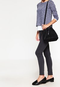 Svart handväska i mocka med en axelrem, kompletterad med en texturerad blå tröja, grå smala jeans och glänsande svarta ballerinaskor.