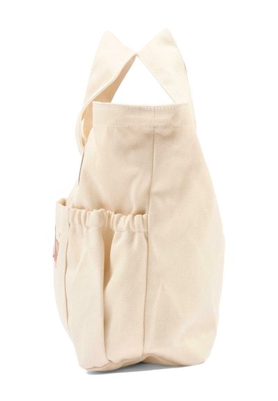 Beżowa torba typu tote z płótna z szerokimi paskami i elastyczną boczną kieszenią, pokazana z boku na białym tle.