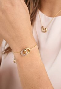 Guldkedja med sammanfogade cirkulära länkar, en med rosa stenar, fäst vid en delikat kedja med en liten berlock.