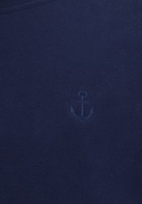 Marineblå strikket sweater med et diskret broderet ankerlogo. Glat tekstur med en klassisk rund hals.