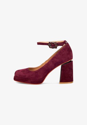 Pump in suede bordeaux con plateau, dotato di un ampio tacco a blocco e una fibbia decorativa sulla cinghia alla caviglia. Texture liscia e design a punta rotonda.