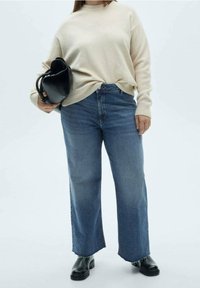 Suéter de punto beige, jeans de tiro alto, anchos y azules, botas de cuero negras hasta el tobillo y un bolso negro. Detalles de un atuendo simple y moderno.