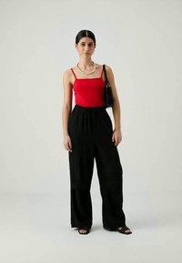 Punane sobiv tank top, mustad laiad püksid, pärlikee ja must käekott. Mudel seisab neutraalses taustas.