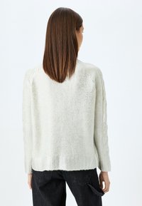 Helles silbernes Sweatshirt mit einem strukturierten Strickdesign, geripptem Saum und Kabelstrickakzenten an den Ärmeln; getragen mit dunklen Jeans.