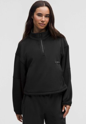 Czarna bluza z polaru z suwakiem do połowy, o luźnym kroju, z wysokim kołnierzem i haftowanym logo na piersi. Posiada długie rękawy zakończone mankietami.