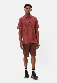 Korte mouwen, rood geruit overhemd met een zak, gecombineerd met bruine cargoshorts. Draag het met zwarte sneakers en gestreepte sokken. Minimale achtergrond.