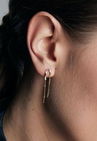 Złote kolczyki w kształcie obręczy charakteryzują się minimalistycznym wzornictwem z delikatnie zwisającymi łańcuszkami. Gładka tekstura i polerowane wykończenie podkreślają ich elegancję.