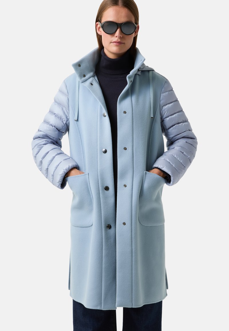 Světle modrý kabát s fleecovým tělem a prošívanými rukávy. Obsahuje kapuci, patentky a dvě přední kapsy. Hladký povrch po celé ploše.