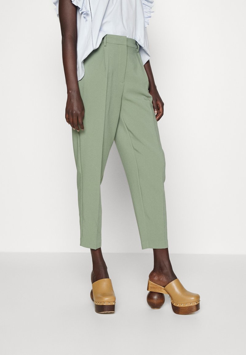 Haut bleu clair à volants associé à un pantalon vert taille haute ajusté et des sabots marron avec une base en bois rond et des clous en métal.