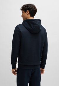 Sweatshirt azul-marinho feito de material macio, apresentando um bolso canguru, capuz com cordão e punhos e bainha canelados. Design simples e sem emendas.