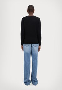 Maglione nero lavorato a maglia con maniche lunghe, abbinato a jeans a gamba larga blu chiaro, che mostra un design semplice e pulito dal retro.