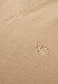 Sweatshirt en coton beige avec une surface texturée, un col ribbed et un logo "Super Dry" brodé sur la poitrine.