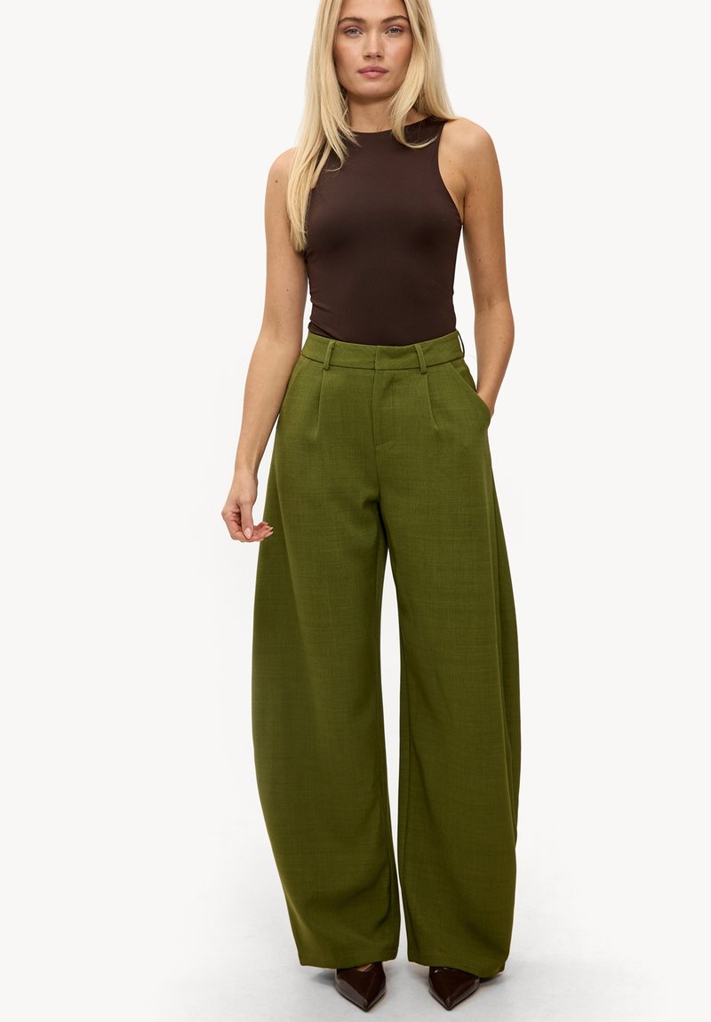 Pantalon vert à jambes larges en tissu texturé, associé à un haut marron ajusté sans manches. Il comporte des plis à l'avant et une taille ceinturée.