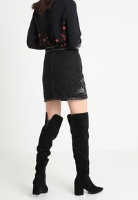 Svarta mocka stövlar över knäet med klack, i kombination med en svart denimkjol med blommig brodyr.