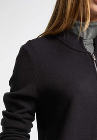 Svart zip-up-tröja med mjuk textur och hög krage, med ett grått innerfoder och åtsittande, uppvikta ärmar.