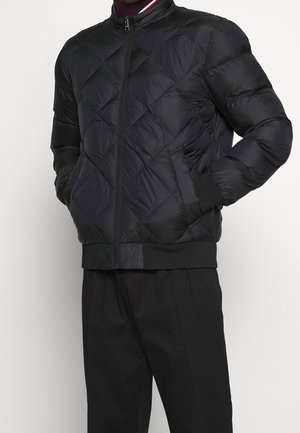 Chaqueta acolchada negra de tejido sintético con cremallera frontal, puños de canalé y diseño de cuello redondo.