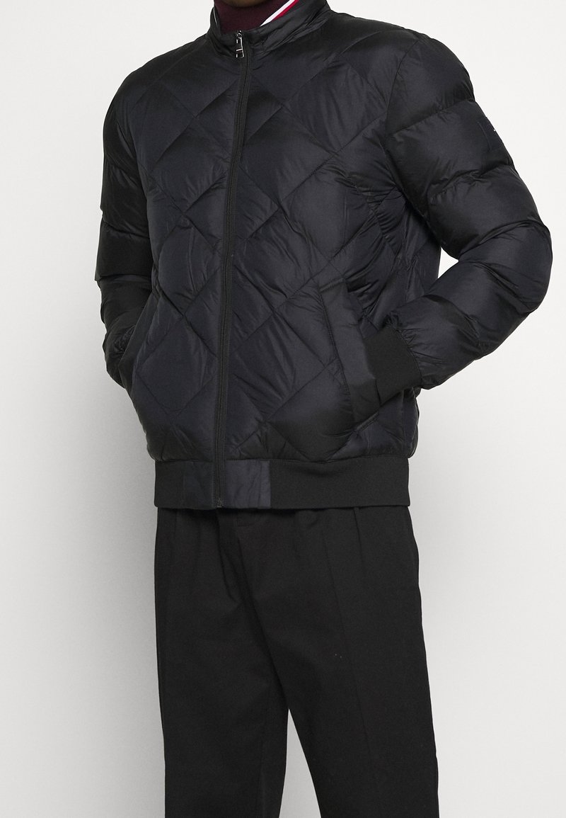 Giacca imbottita nera trapuntata realizzata in materiale sintetico, con zip frontale, polsini a coste e design con collo rotondo.