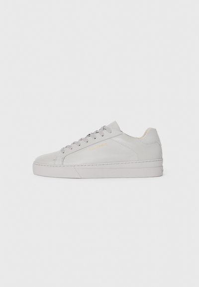 Baskets en cuir gris clair avec une texture lisse, bout arrondi, semelle en caoutchouc plate et lacets ton sur ton. Présente un minimalisme de la marque en doré.