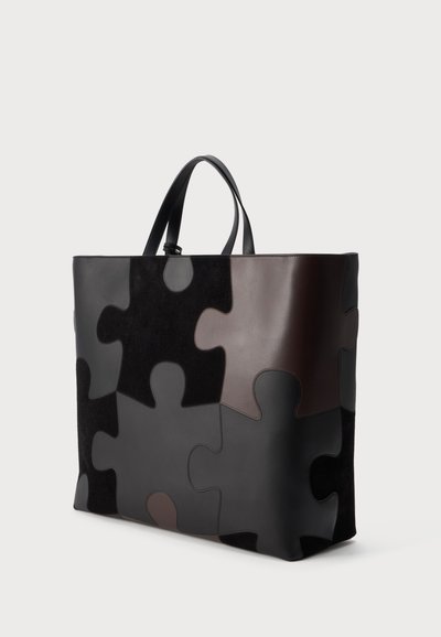 Grand sac cabas avec motif de pièces de puzzle dans des tons noirs et marron, texture en cuir lisse, deux poignées noires, debout.