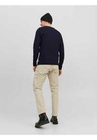 Tumes tekstuuriga kampsun, beežid püksid, mustad saapad ja müts. Riietus on lõdva lõikega ja minimalistliku disainiga, andes sellele juhusliku ilme.