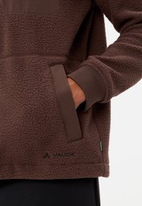 Pullover in fleece marrone con superficie testurizzata, dettagli di accento marrone contrastanti su tasche e polsini, con un piccolo logo verde.