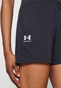Mustat urheilushortsit, jotka on valmistettu puuvillasekoitekankaasta. Niissä on joustava vyötärö ja valkoinen Under Armour -logo vasemmassa reidessä.