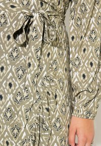 Vestido verde con estampado que presenta una cintura ajustable, con intrincados diseños en blanco y negro, tejido ligero y detalles de mangas fruncidas.
